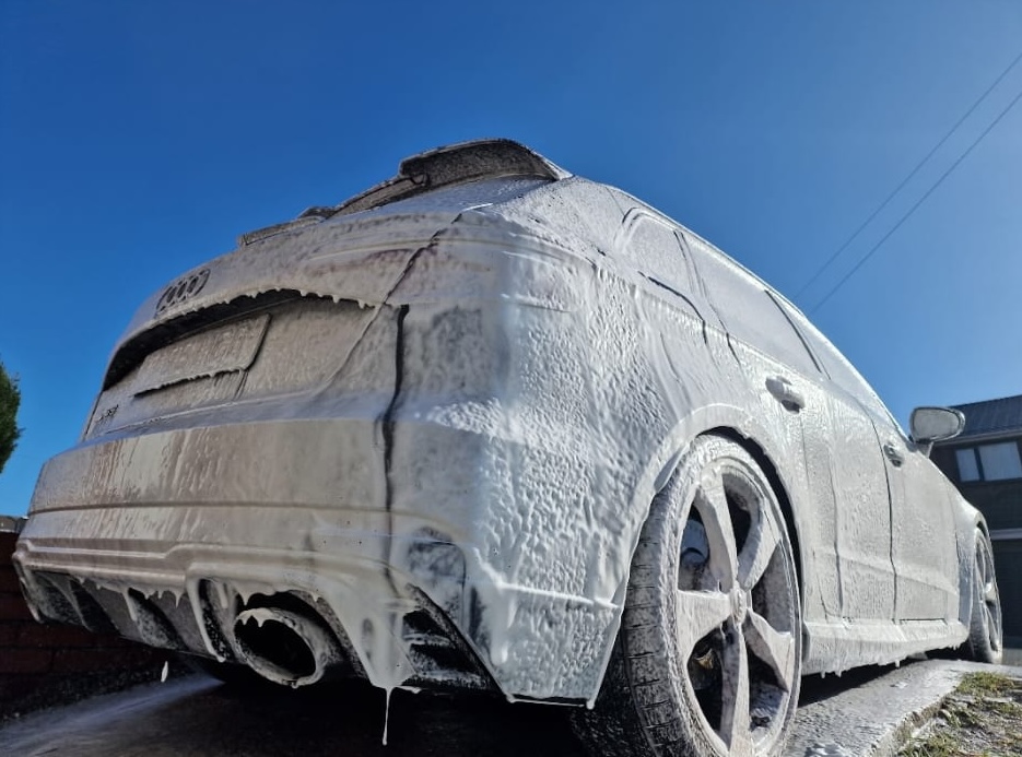 Audi RS3 covered in thick snow foam suds during a safe pre-wash under blue sky