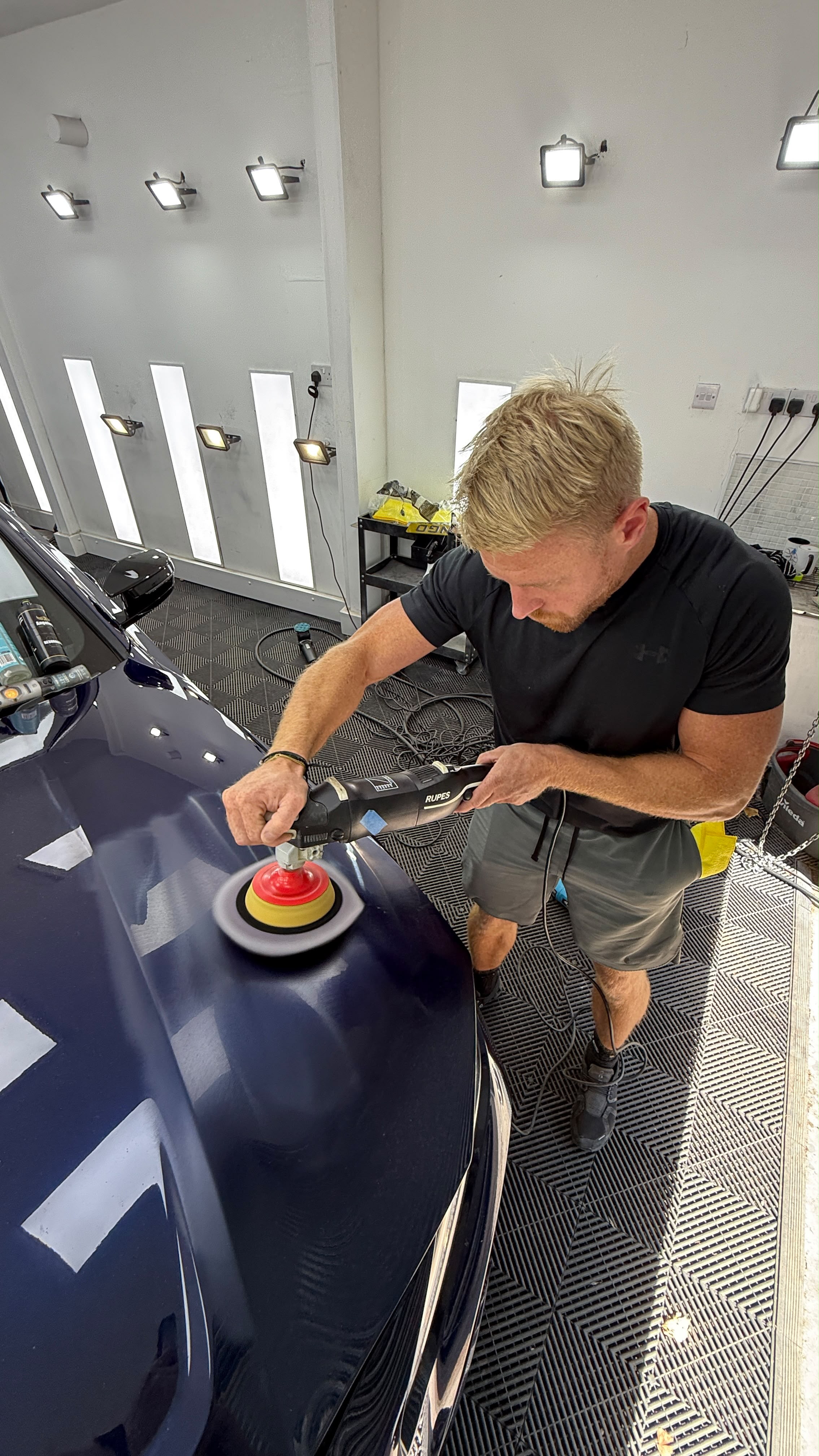 Detailer machine polishing a navy bonnet with a RUPES rotary polisher in the studio